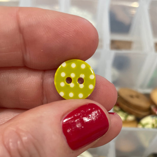 Hand holding a yellow button with white polka dots in front of a container of buttons.