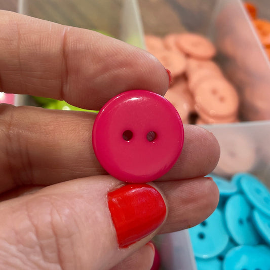 Hand holding a pink button with containers of buttons in the background