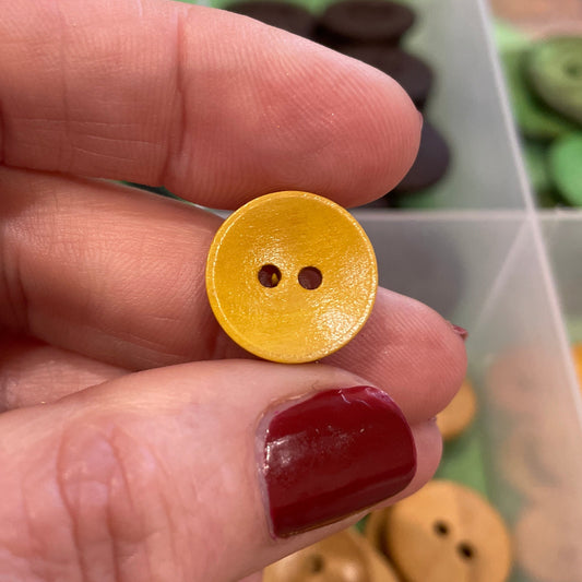 Gold button held between fingers with a container of buttons in the background