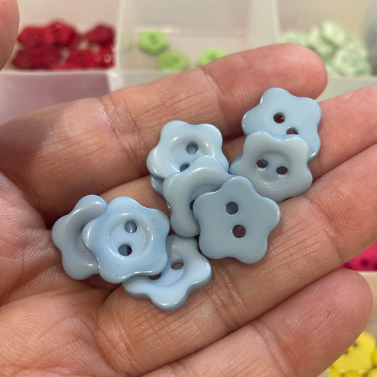 Hand holding light blue flower-shaped buttons with a blurred background of colorful buttons.