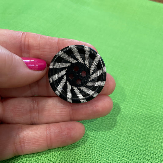 Hand holding a black and white patterned button against a green background