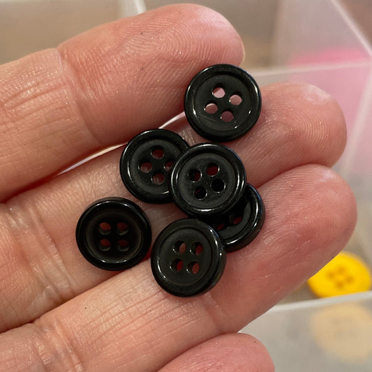 Black buttons held in a hand with a container of colorful buttons in the background