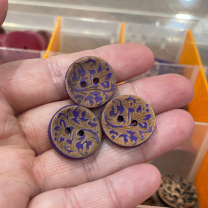 Hand holding three decorative buttons with a blurred background of a button collection.