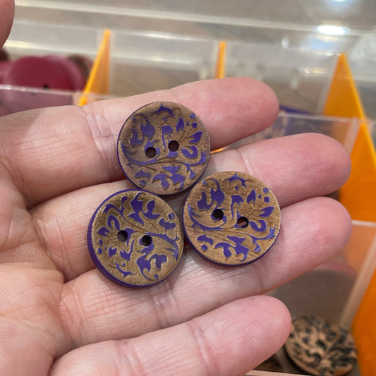 Hand holding three decorative buttons with a blurred background of a button collection.
