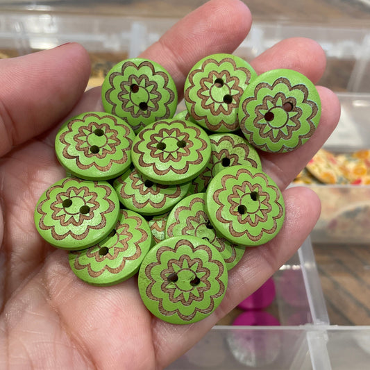 Hand holding green floral-patterned buttons with a blurred background of more buttons and a cityscape.