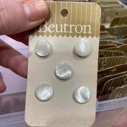 Card with four pearl buttons held by a hand, brand 'beutron' visible