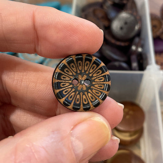 Hand holding a decorative button with a blurred background of button collection