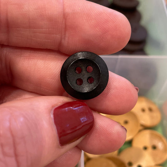 Hand holding a black button with a container of wooden buttons in the background