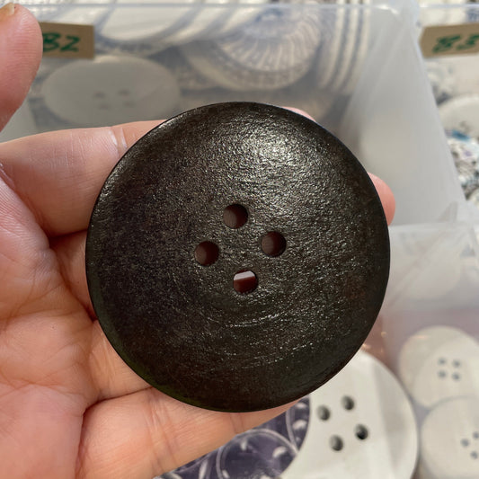 Hand holding a large black button with a blurred background of buttons