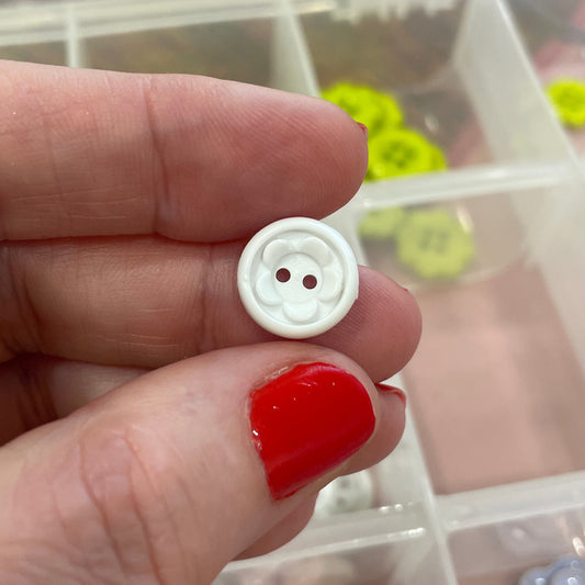 Hand holding a white button with a clear container of buttons in the background