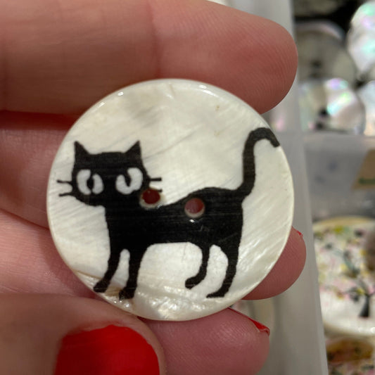 Button with a black cat design held by a hand against a background of similar buttons.