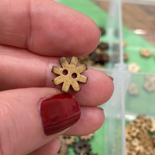 Gold flower-shaped button held between fingers with a container of similar buttons in the background.