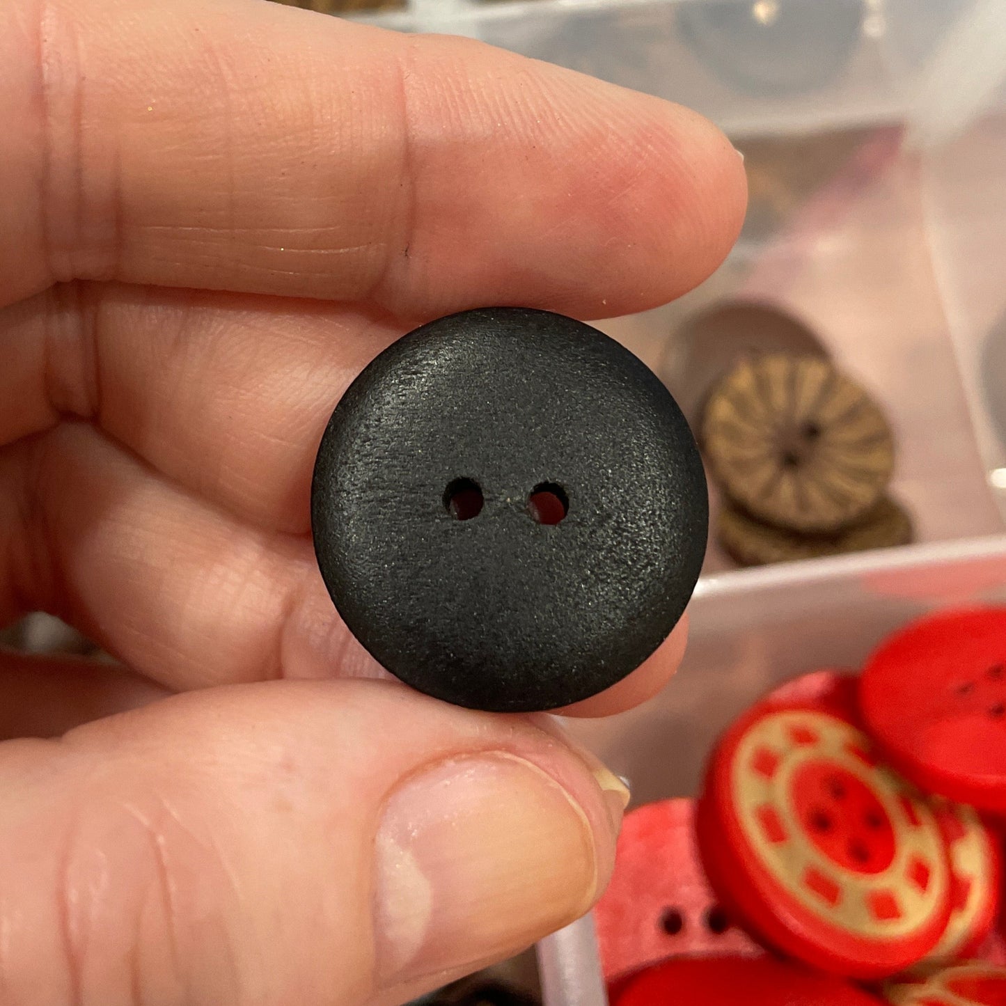 Black button held by a hand with a container of buttons in the background