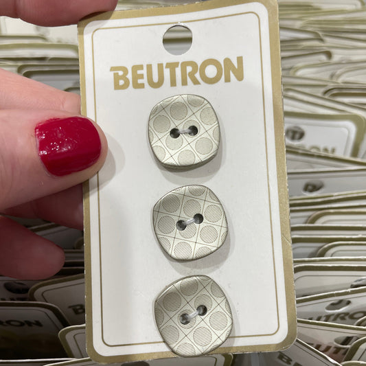 Three silver buttons on a BEUTRON branded card held by a hand with red nail polish.