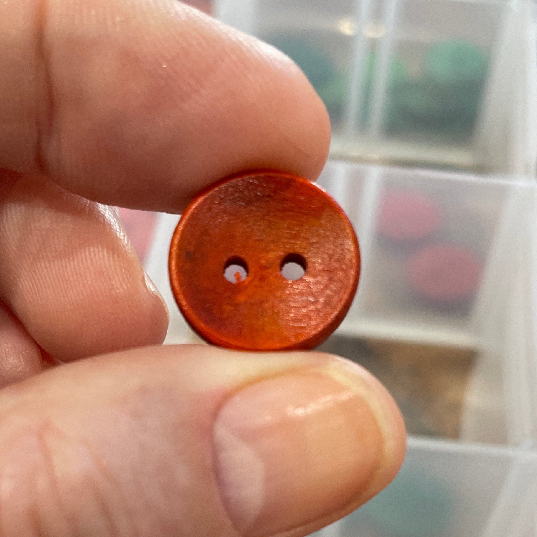 Hand holding a brown button with a clear container of buttons in the background