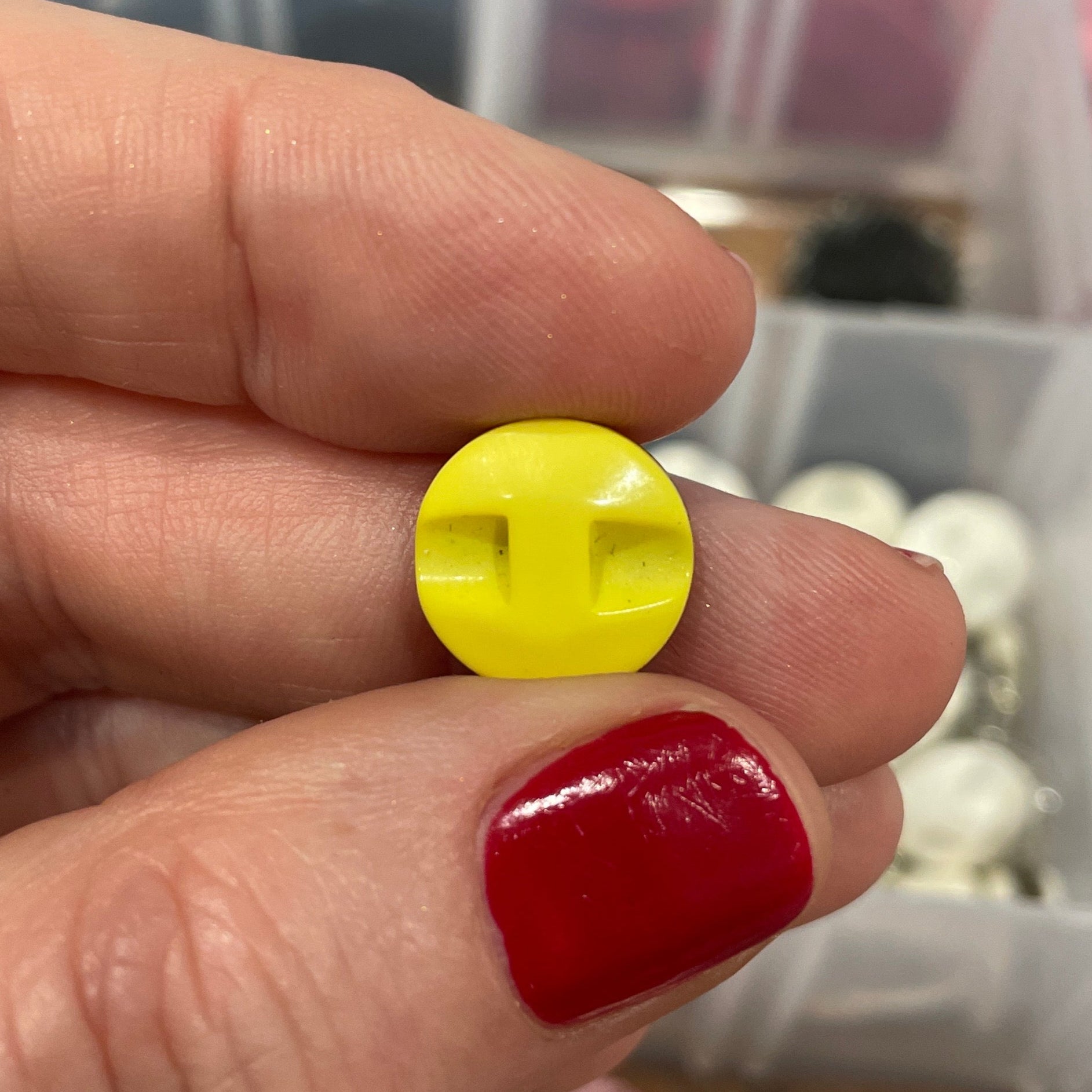 Hand holding a yellow button with a blurred background of a container with various buttons.