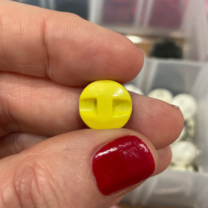 Hand holding a yellow button with a blurred background of a container with various buttons.