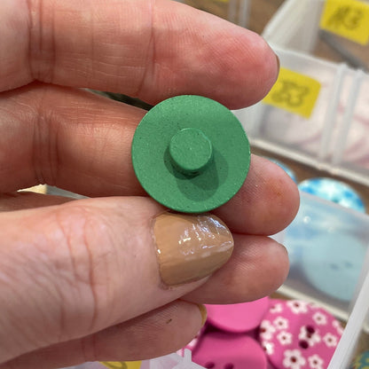 Hand holding a green button with a container of assorted buttons in the background