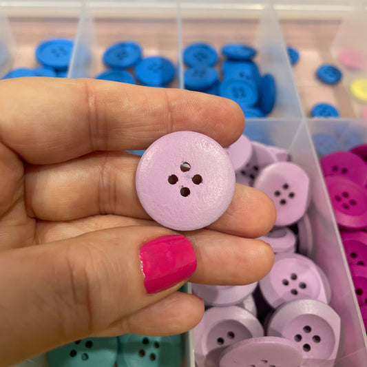 Hand holding a pink button with a colorful button collection in the background