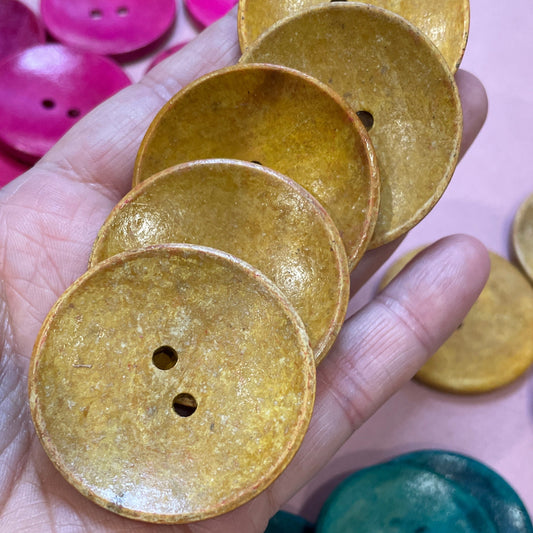 Gold and green buttons on a hand with a pink background