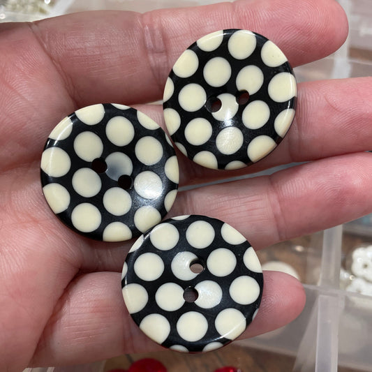 Black and white polka dot buttons held in a hand with a container of red buttons in the background.