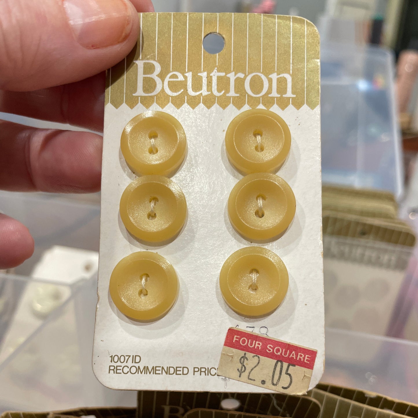 Packaging of beige buttons with 'Beutron' branding held by a hand.