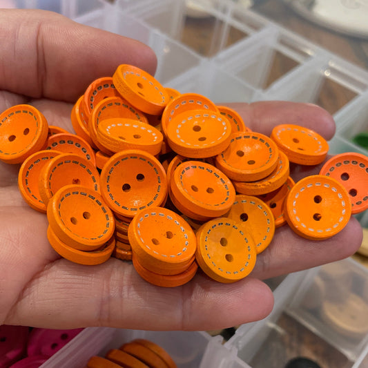 Hand holding a collection of orange buttons with a container of more buttons in the background.