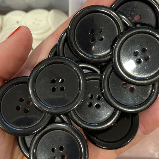 Hand holding a collection of black buttons with a clear container of buttons in the background.