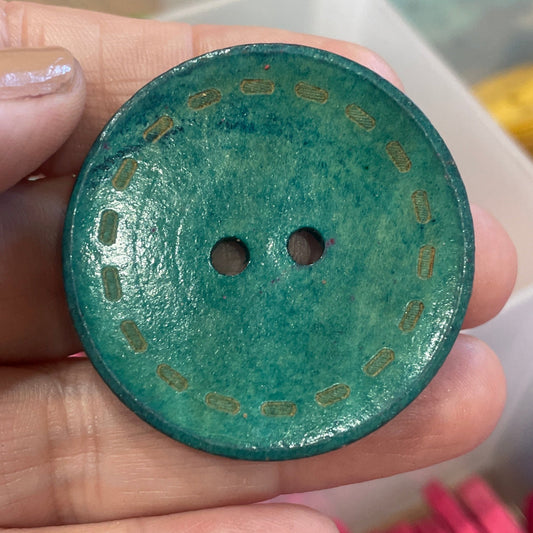 Hand holding a green button with a blurred background of colorful buttons