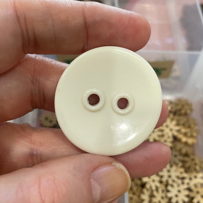 Hand holding a white button with a blurred background of small metal gears.