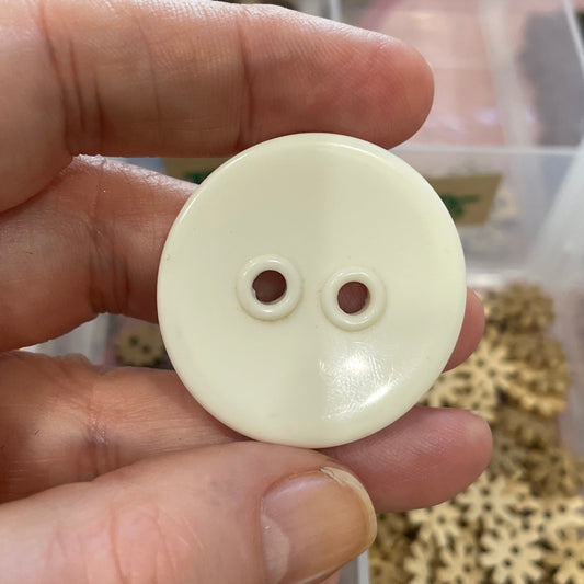 Hand holding a white button with a blurred background of small metal gears.
