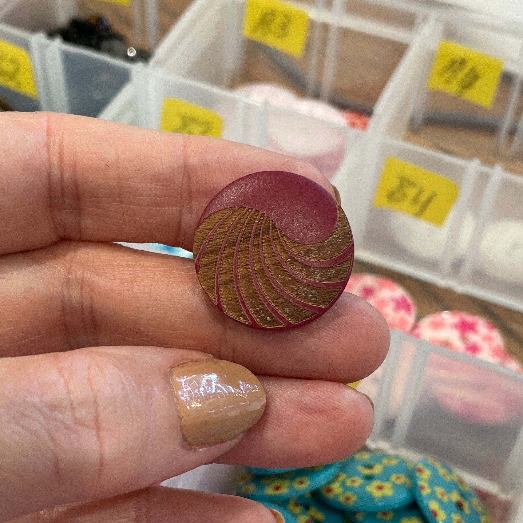 Hand holding a button with a container of various buttons in the background