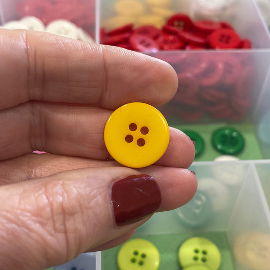 Hand holding a yellow button with a container of assorted buttons in the background