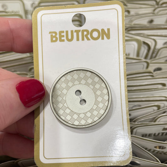 Beutron button packaging held by a hand with red nail polish, with more packaging in the background.