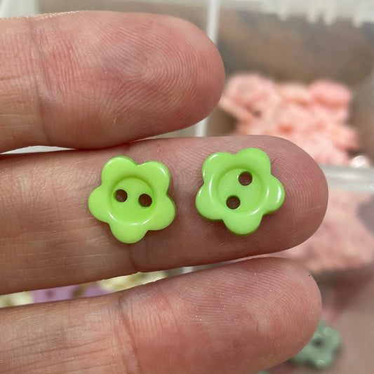 Hand with green flower-shaped buttons on fingers, blurred container of buttons in the background
