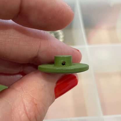 Hand holding a green button with a container of buttons in the background