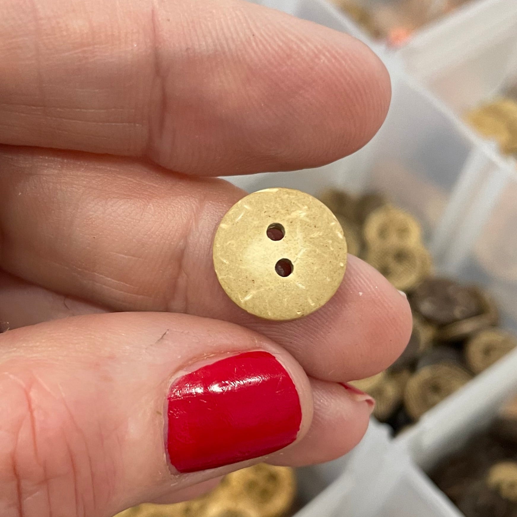 Button held between fingers with a container of buttons in the background
