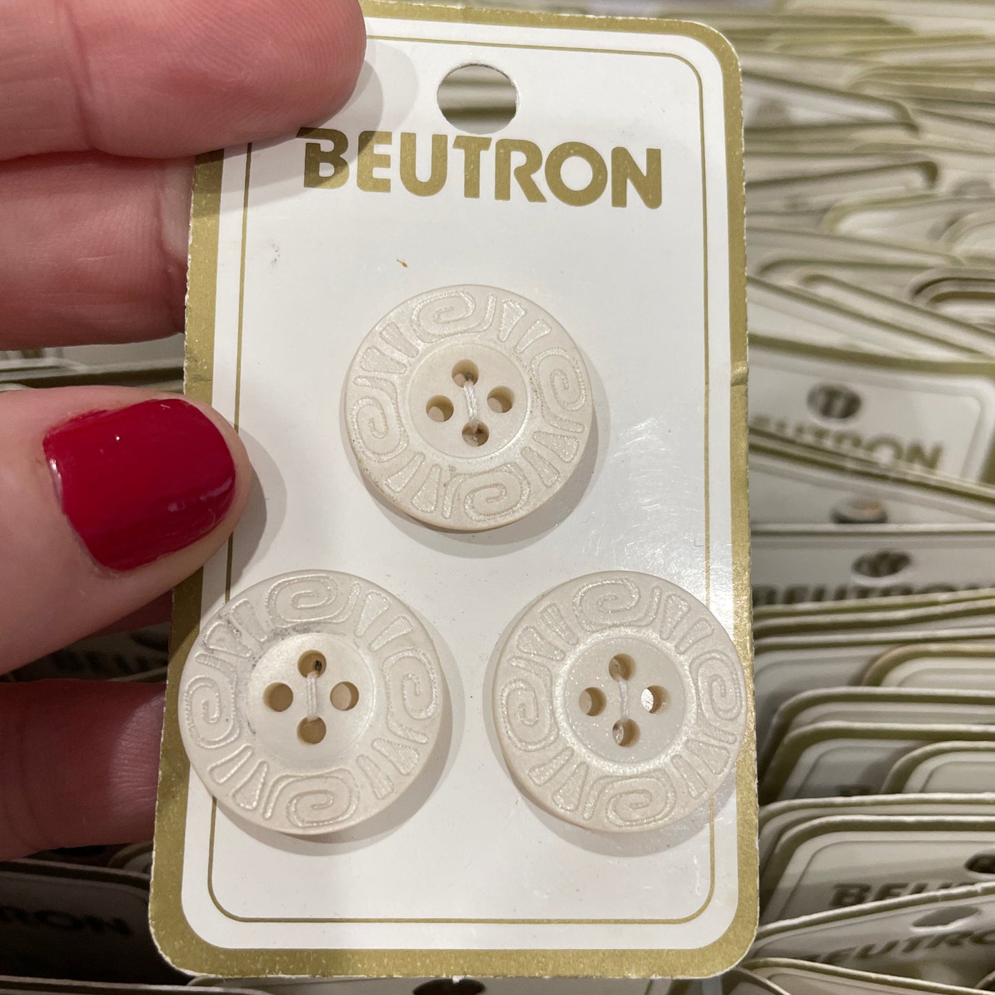 Beutron buttons on a card held by a hand with red nail polish.