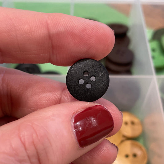 Hand holding a black button with a container of buttons in the background