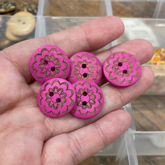 Hand holding pink decorative buttons with a container of various buttons in the background.