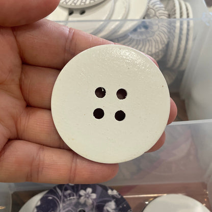 White button held in a hand with a display of various buttons in the background