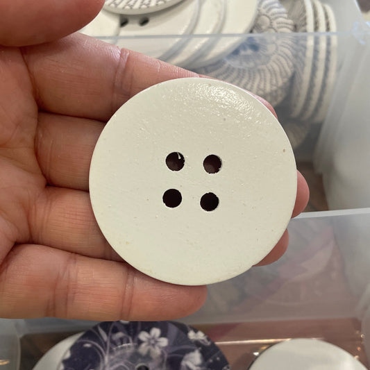White button held in a hand with a display of various buttons in the background