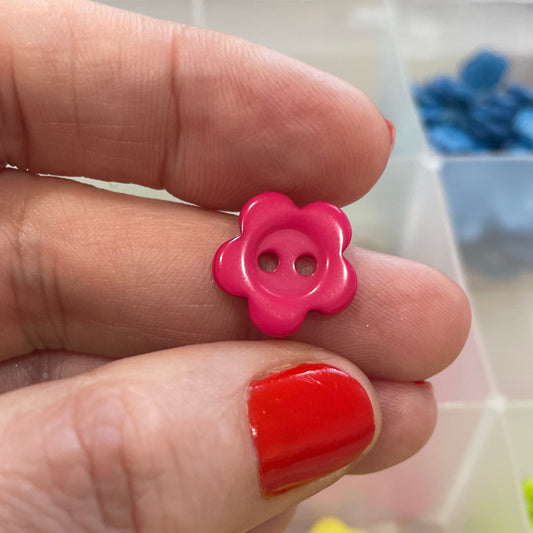Hand holding a pink flower-shaped button with a blurred background of colorful buttons.