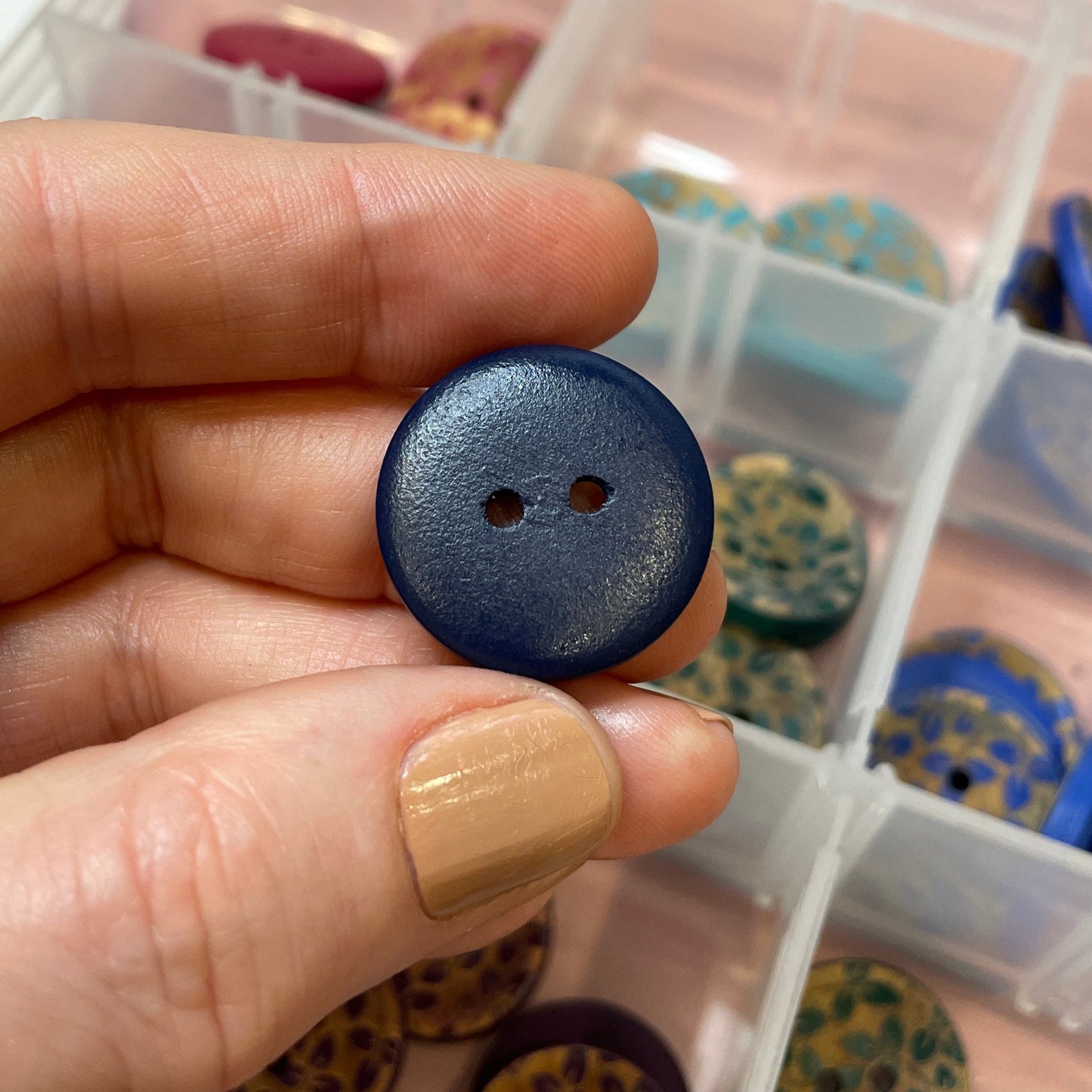Hand holding a blue button with a container of buttons in the background