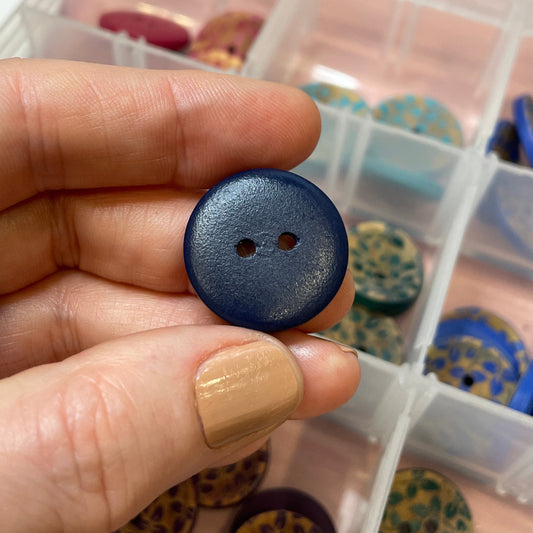 Hand holding a blue button with a container of buttons in the background