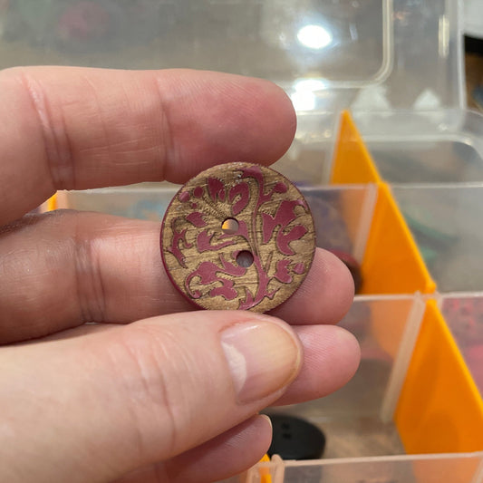 Hand holding a decorative button with a clear container of buttons in the background