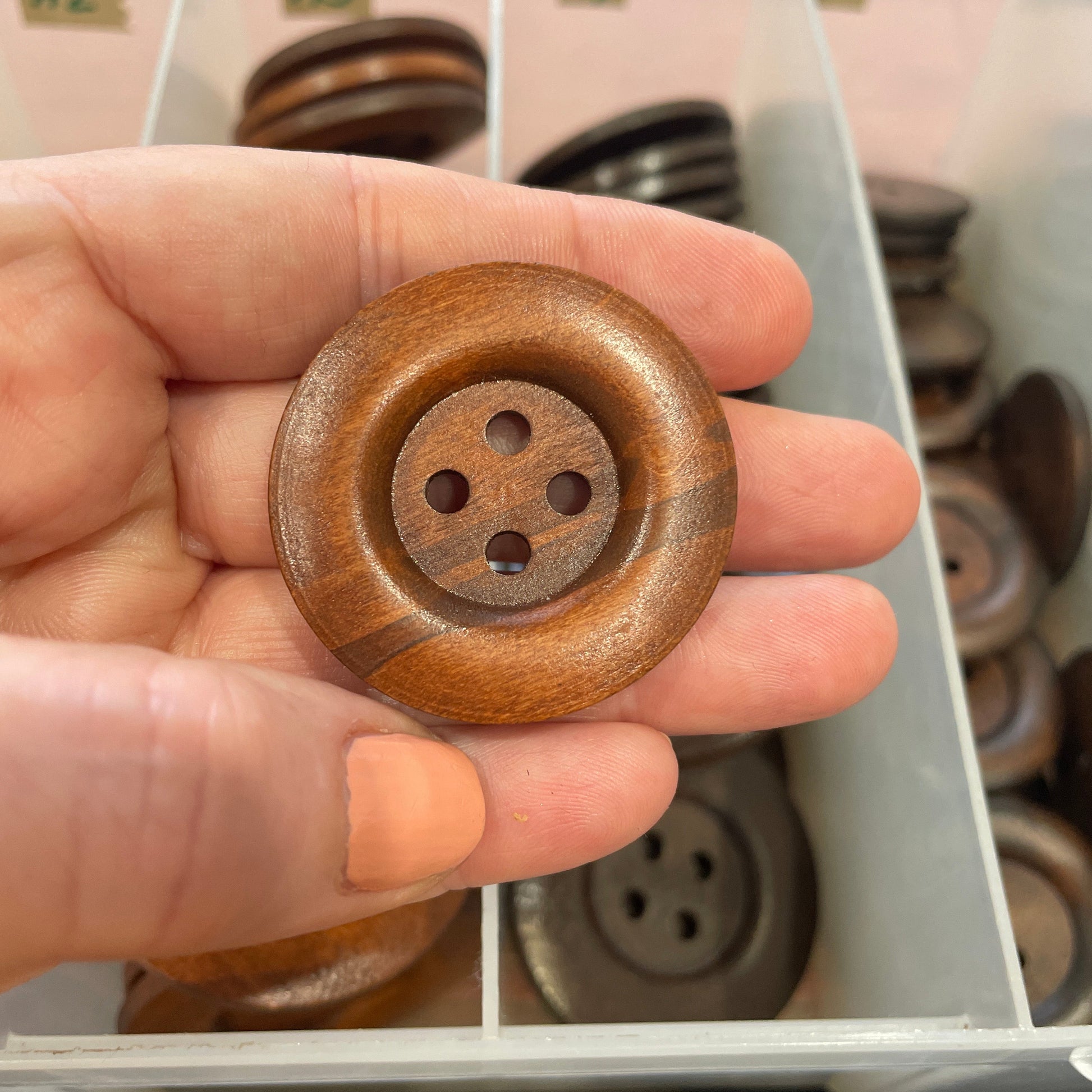Hand holding a wooden button with a blurred background of more buttons.