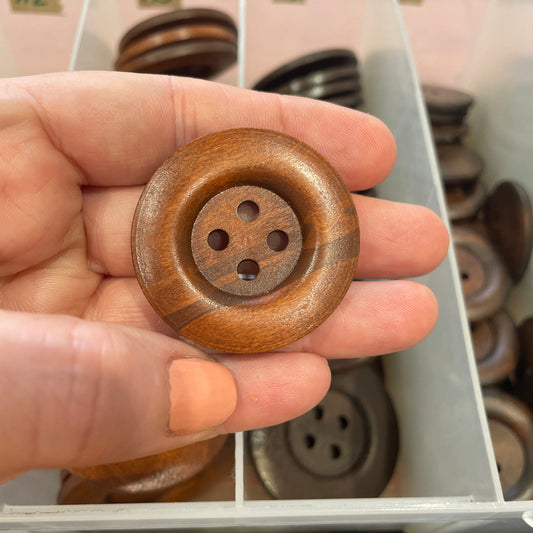 Hand holding a wooden button with a blurred background of more buttons.