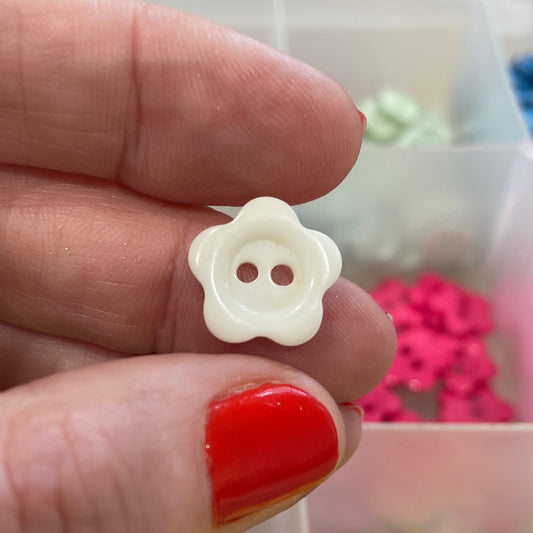 White button with flower design held between fingers, with a container of colorful buttons in the background.
