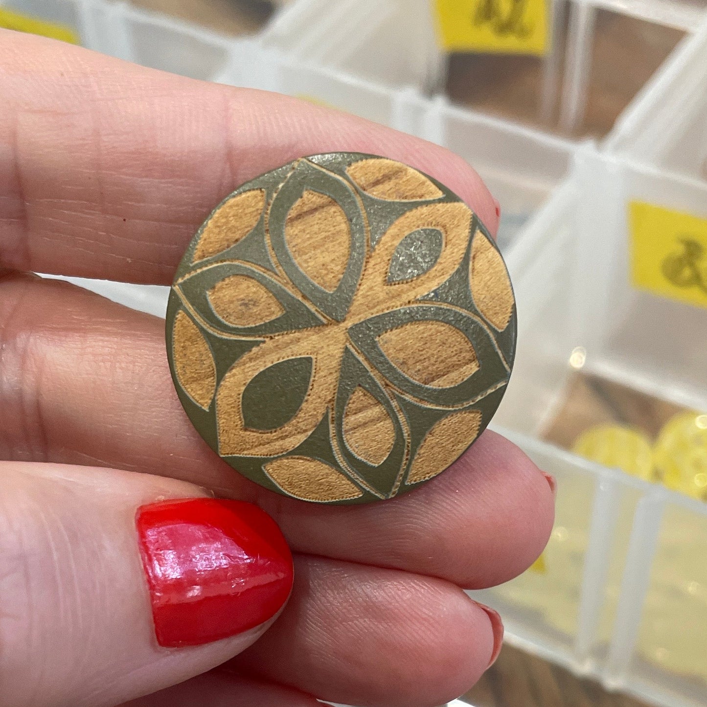 Hand holding a decorative button with a pattern, against a background of a button organizer.